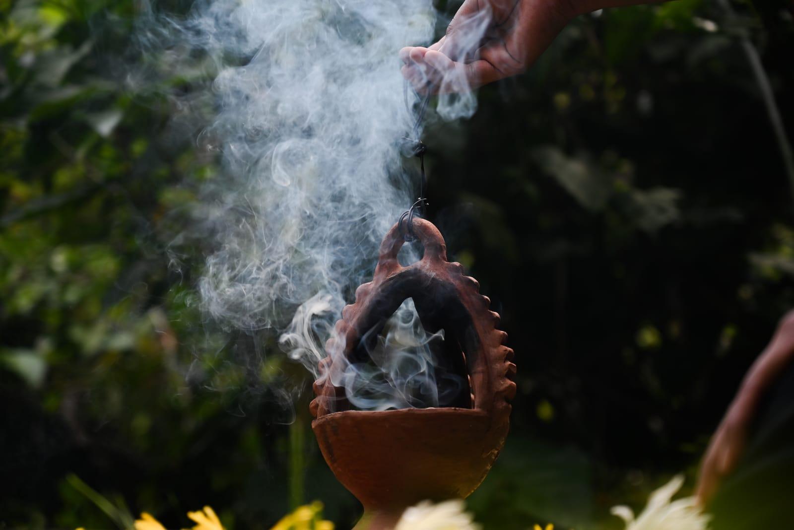 Hands tending a clay copal censer with billowing ceremonial smoke at The Seed
