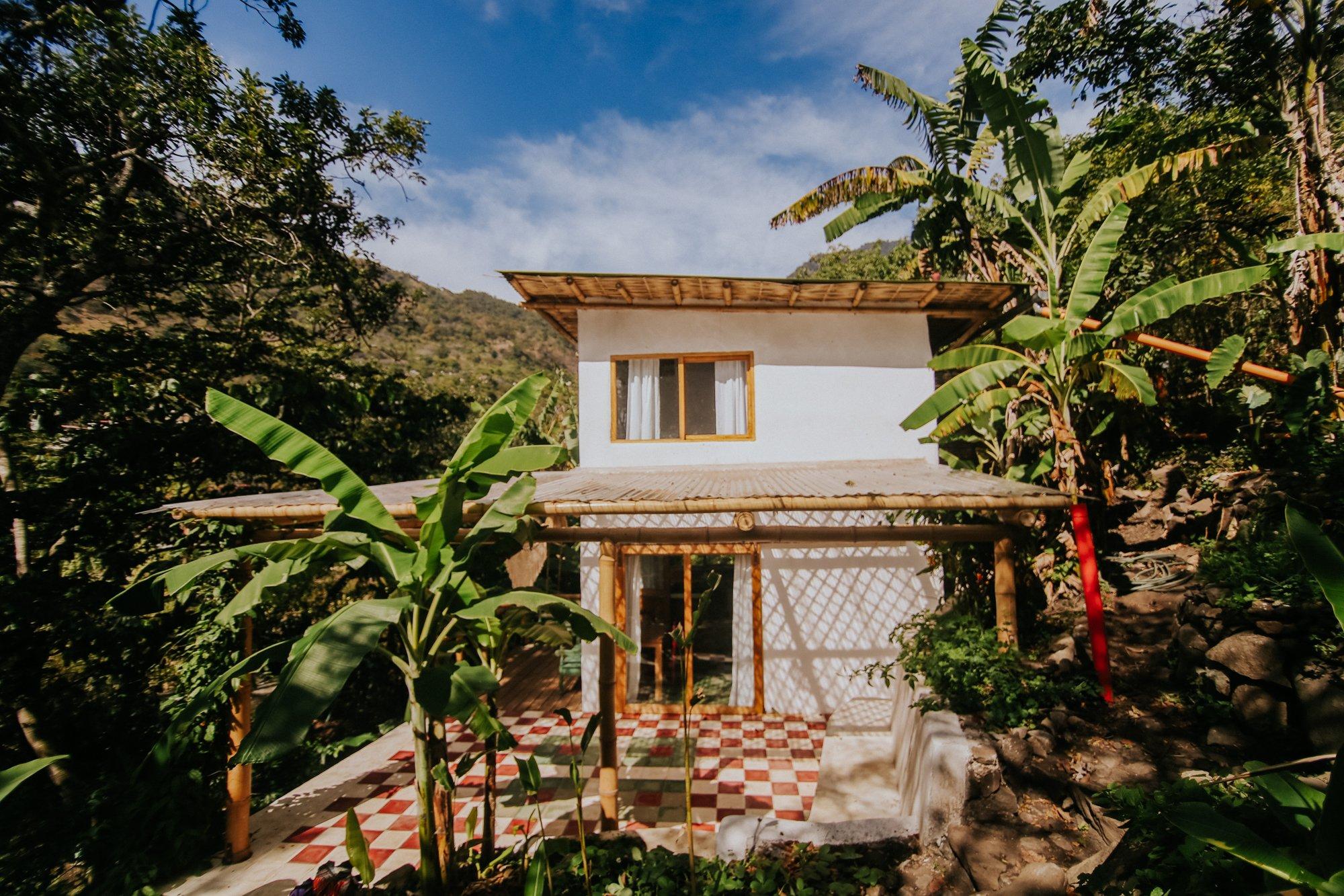 Exterior de Casa Violeta con el edificio blanco, porche de bambú y patio ajedrezado