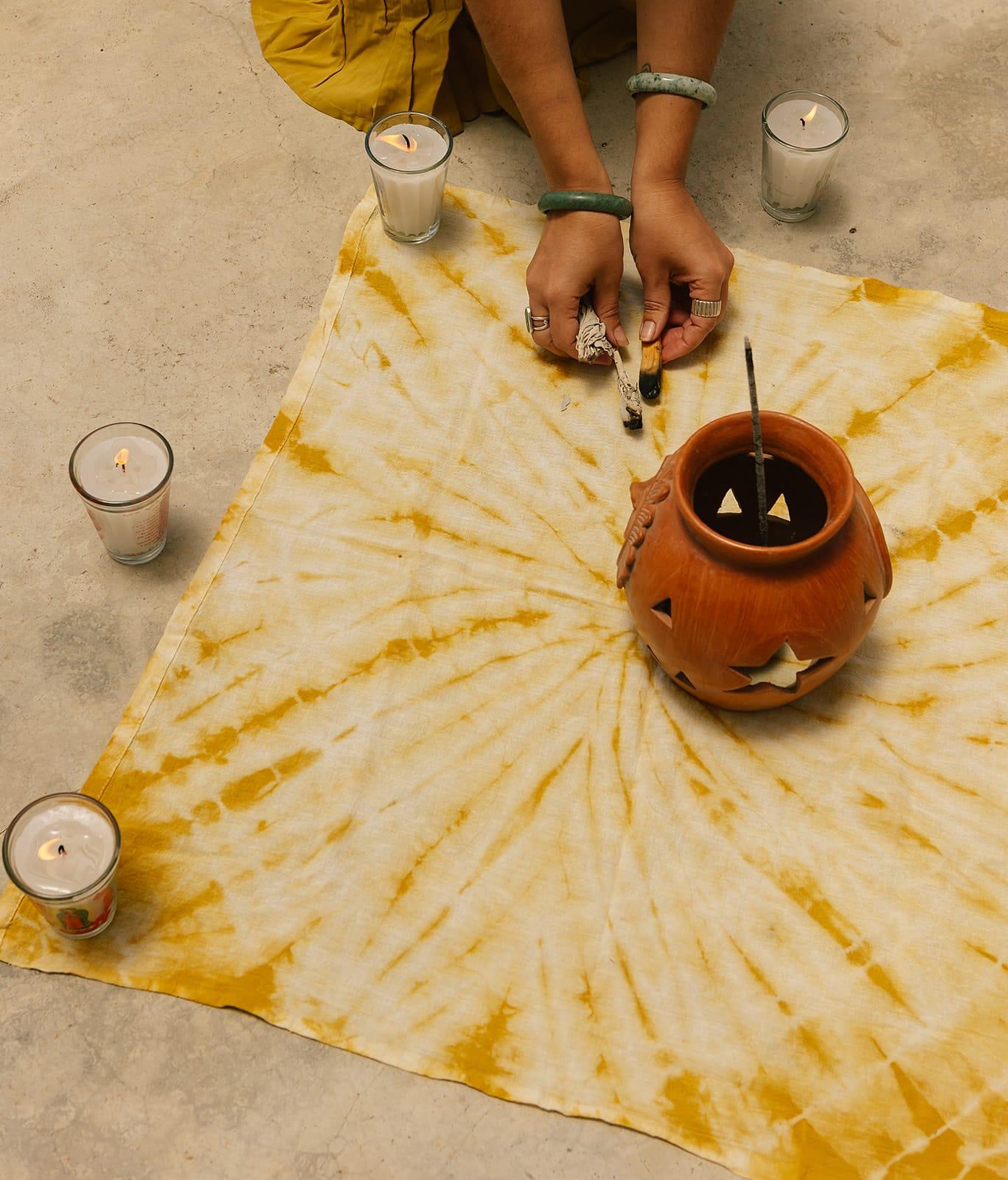 Hands lighting a ceremonial smudge stick beside candles and a clay incense vessel at The Seed